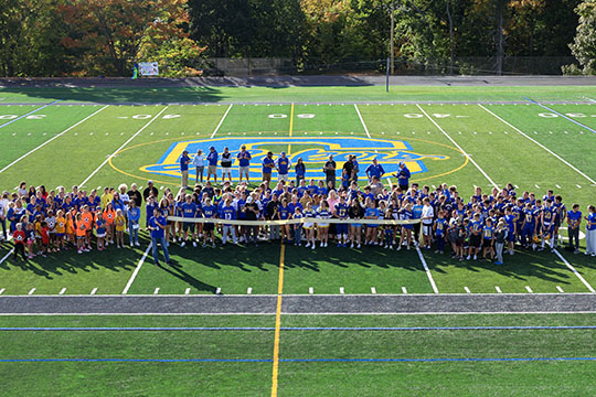 Photo taken  above the field looking down at the teams of athletes holding a yellow ribbon